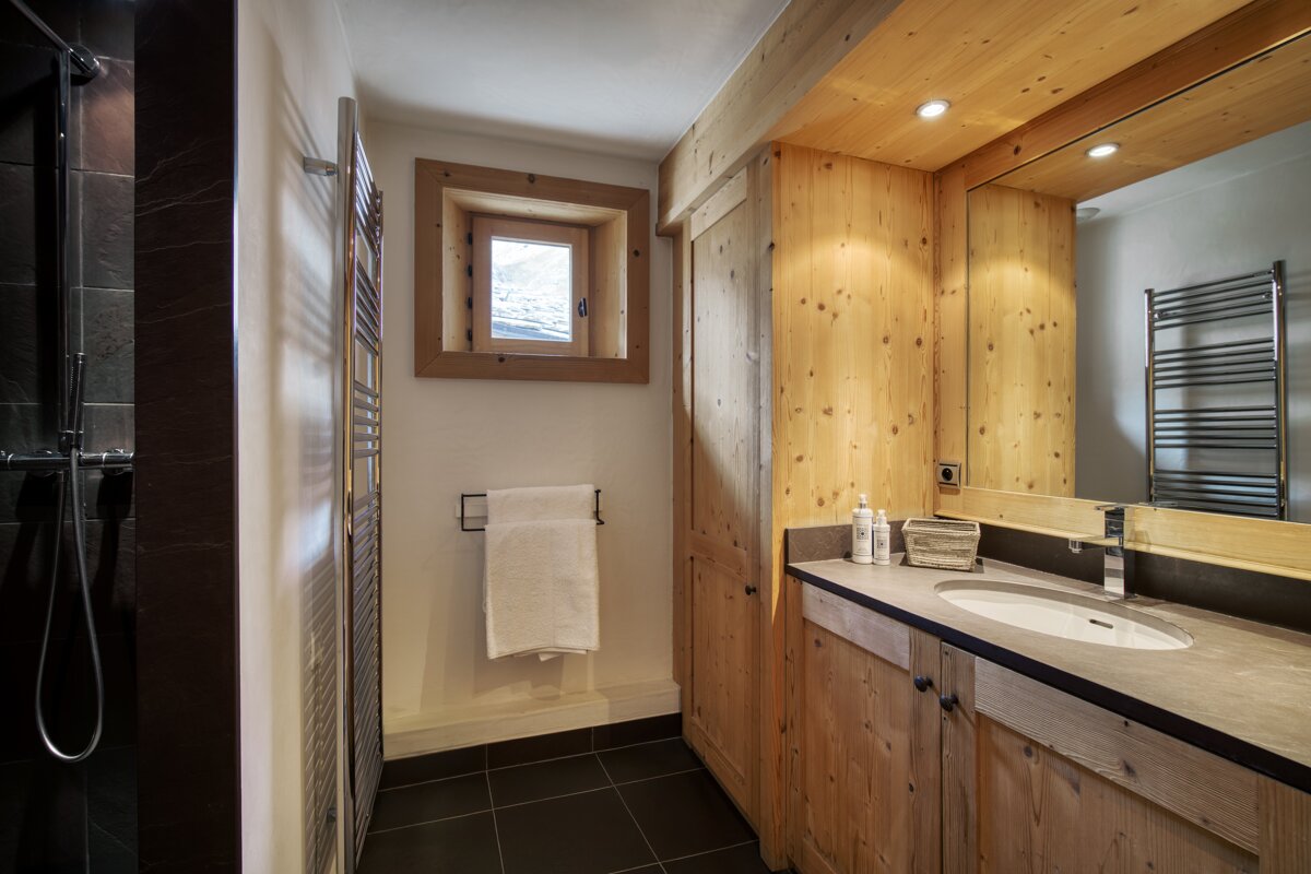 Modern rustic bathroom with warm wood accents, dark tiled shower, a stylish vanity, and a small window.