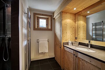 Modern rustic bathroom with warm wood accents, dark tiled shower, a stylish vanity, and a small window.