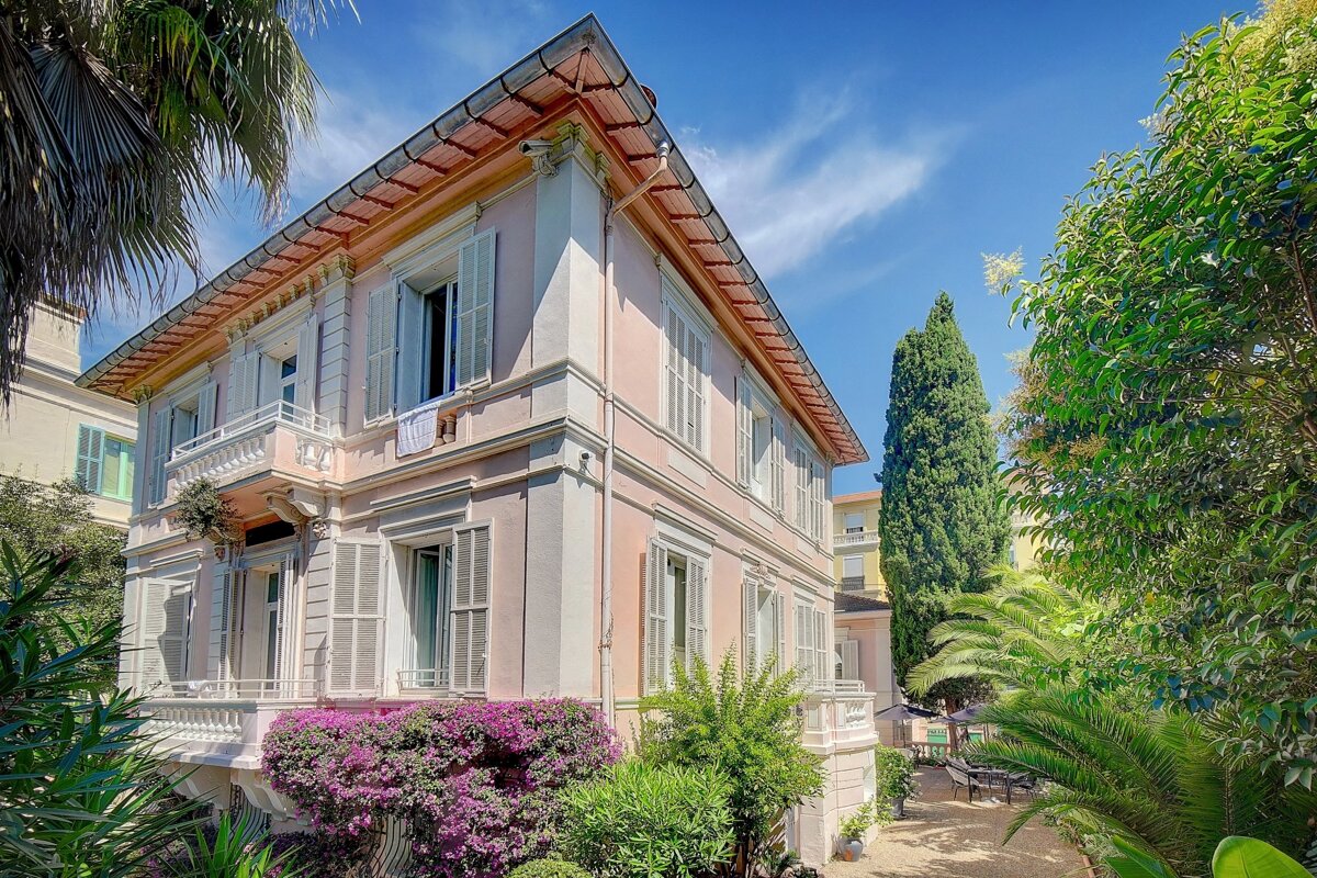 A large house with a balcony and purple flowers in front of it