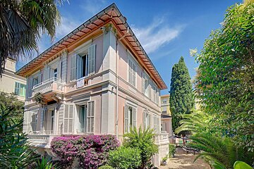 A large house with a balcony and purple flowers in front of it