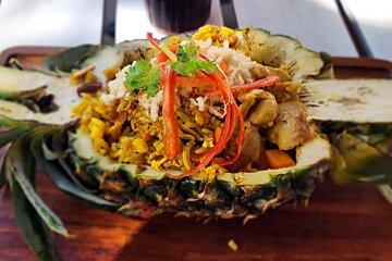 A pineapple filled with rice and vegetables on a wooden table