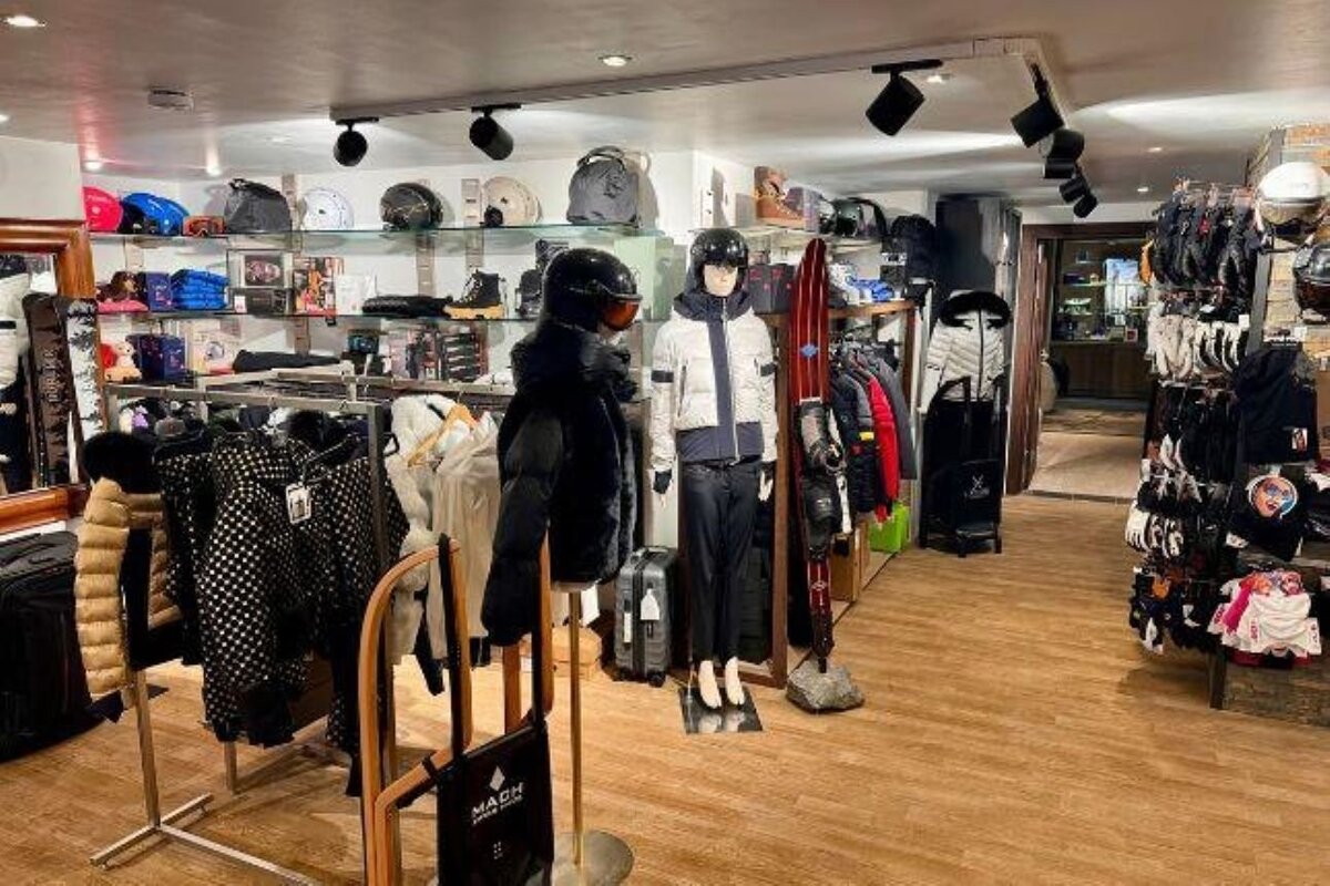 A winter sports shop filled with ski and snowboard gear, helmets, jackets, boots, and clothing displayed on racks and shelves with mannequins.