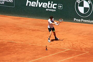 A man playing tennis in front of a helvetic airways sign