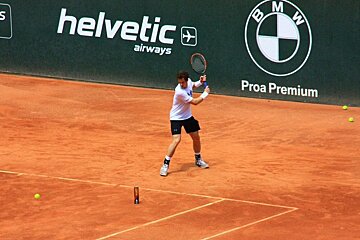A tennis player is swinging a racket on a court sponsored by helvetic airways and proa premium