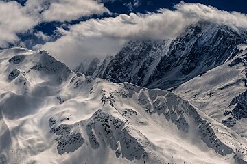 A snowy mountain covered in clouds against a blue sky