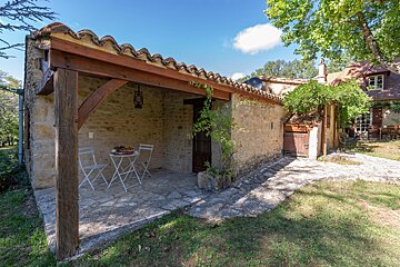 A stone building with a table and chairs under a wooden roof