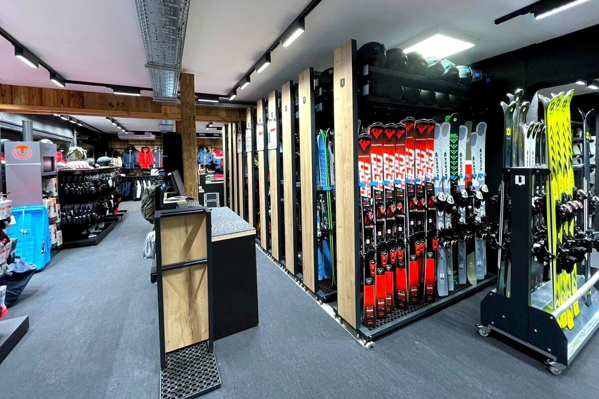A well-lit, modern ski shop displays rows of skis, helmets, and winter gear, ready for sale or rent.