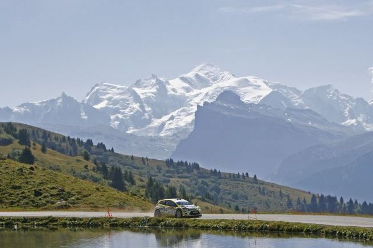 a car going round a lake with month blanc behind