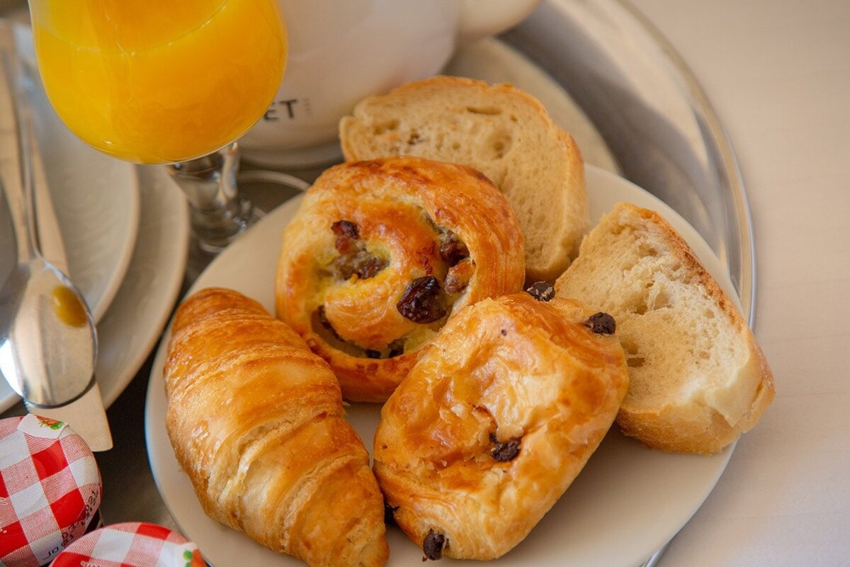 A plate of pastries and bread with a glass of orange juice in the background