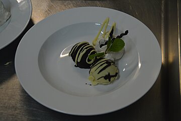 A white plate holds two chocolate truffles (dark and white), a dollop of whipped cream garnished with mint leaves and chocolate curls.