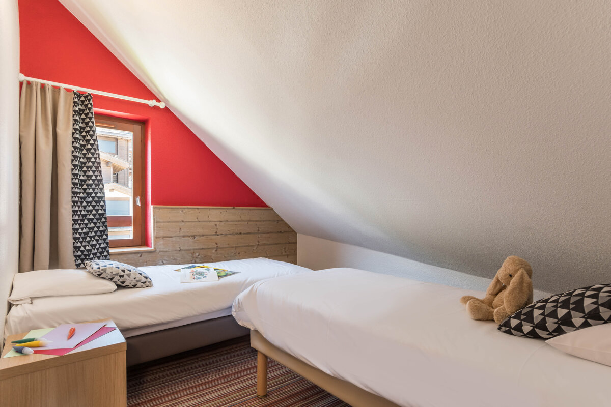 A bedroom with two beds and a teddy bear on the bed