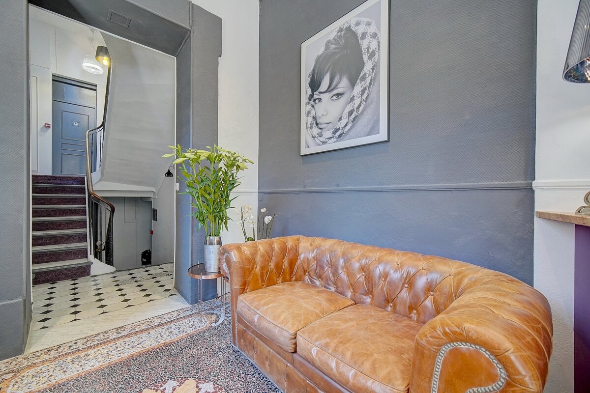 A brown leather couch in a hallway with a picture of a woman on the wall above it