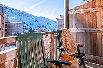 A green chair sits on a balcony overlooking a snowy mountain
