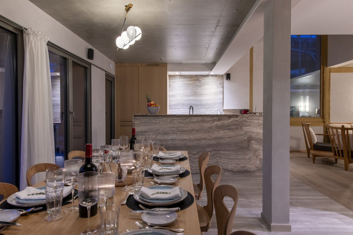 A chic dining room with a set wooden table, modern chandelier, and an elegant kitchen bar area with marble finishes in a contemporary home.