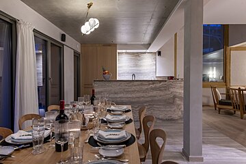 A chic dining room with a set wooden table, modern chandelier, and an elegant kitchen bar area with marble finishes in a contemporary home.
