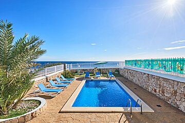 A large swimming pool surrounded by chairs and umbrellas overlooking the ocean