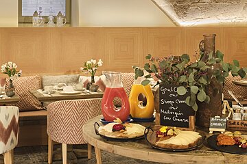 An inviting breakfast spread with various cheeses, colorful juices, and an elegant dining area featuring patterned upholstery and wood panels.