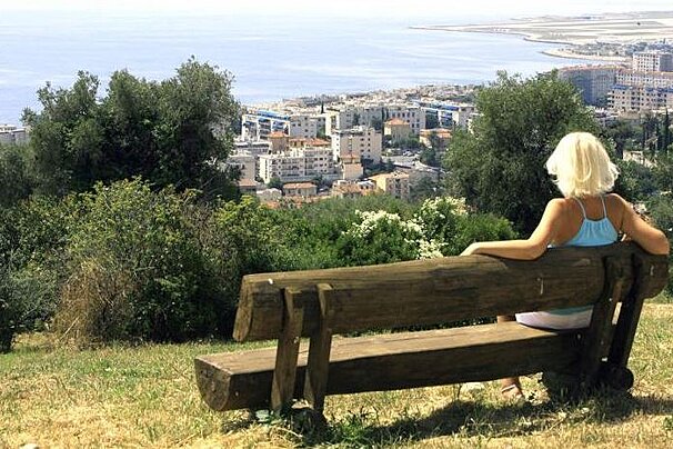 A woman sits on a wooden bench overlooking a city
