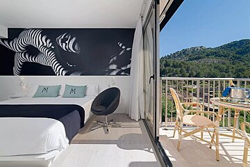 A modern hotel room with a large black-and-white art mural above the bed, a swivel chair, and a balcony offering mountain and valley views with a champagne bucket.