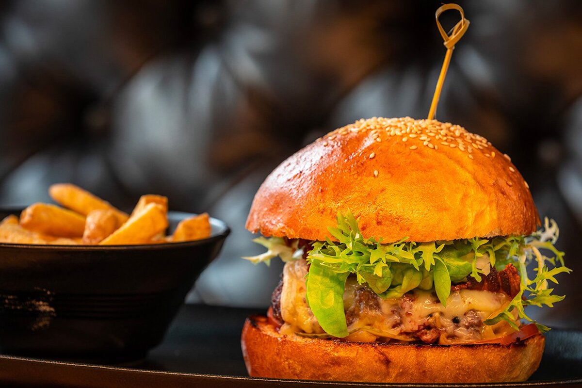 A hamburger on a plate next to a bowl of french fries