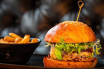 A hamburger on a plate next to a bowl of french fries