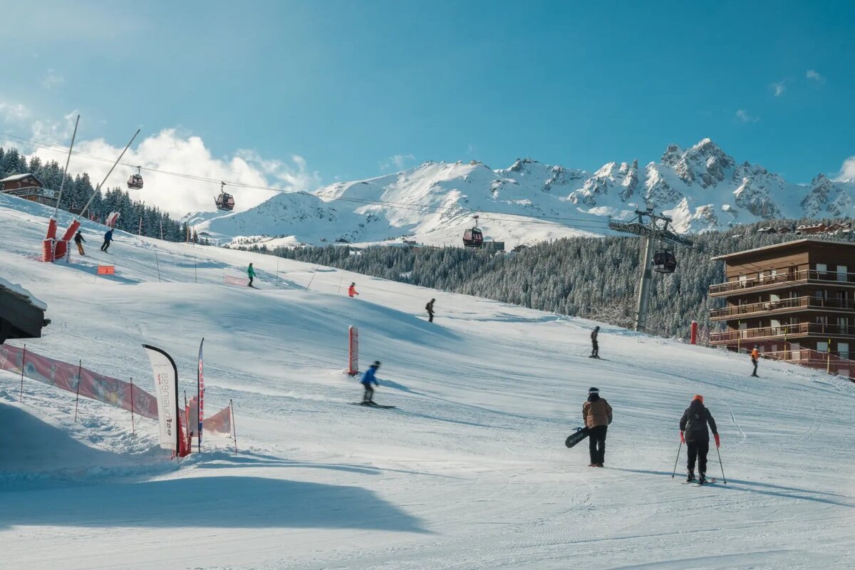 People skiing down a snow covered slope with mountains in the background
