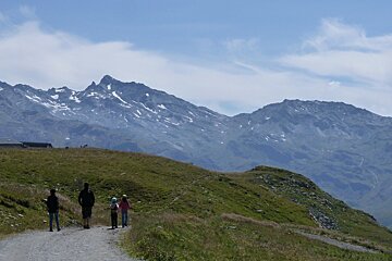 A group of people walking down a dirt path with mountains in the background
