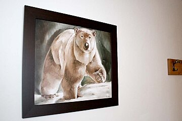 A painting of a polar bear is framed on a white wall