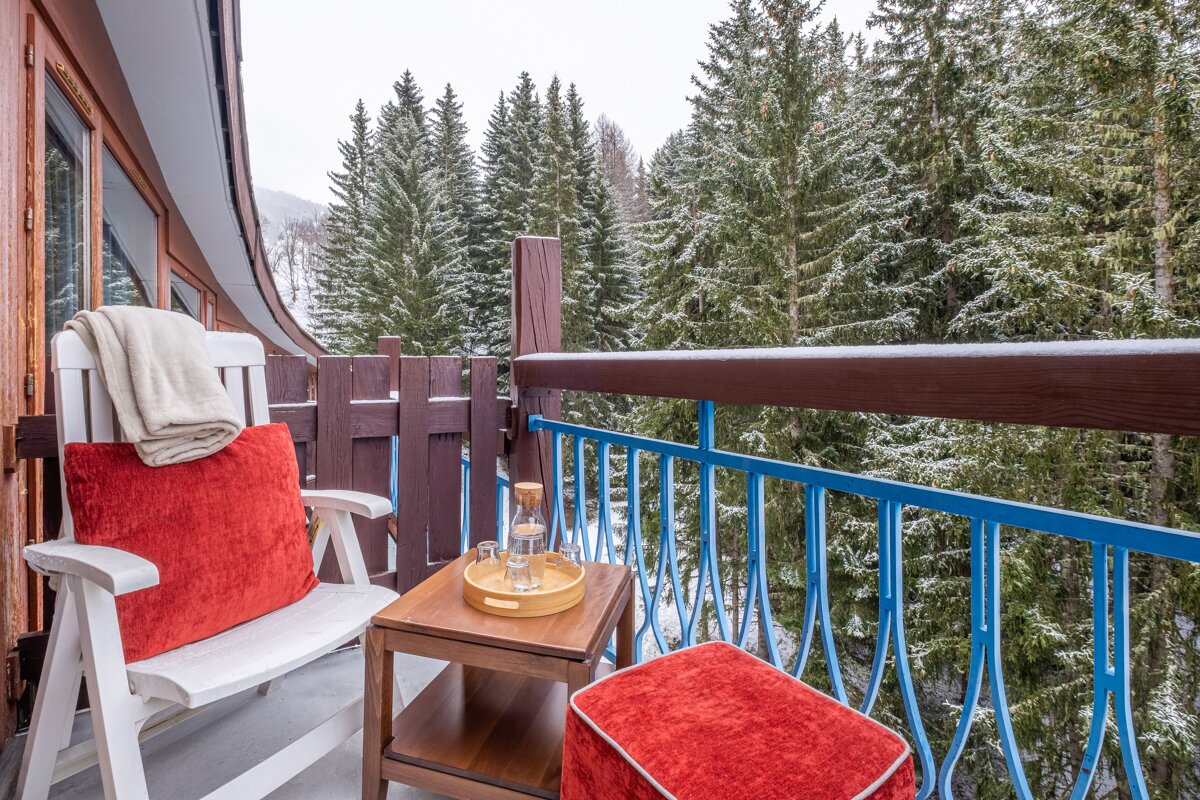 A chair with a red pillow sits on a balcony overlooking a snowy forest