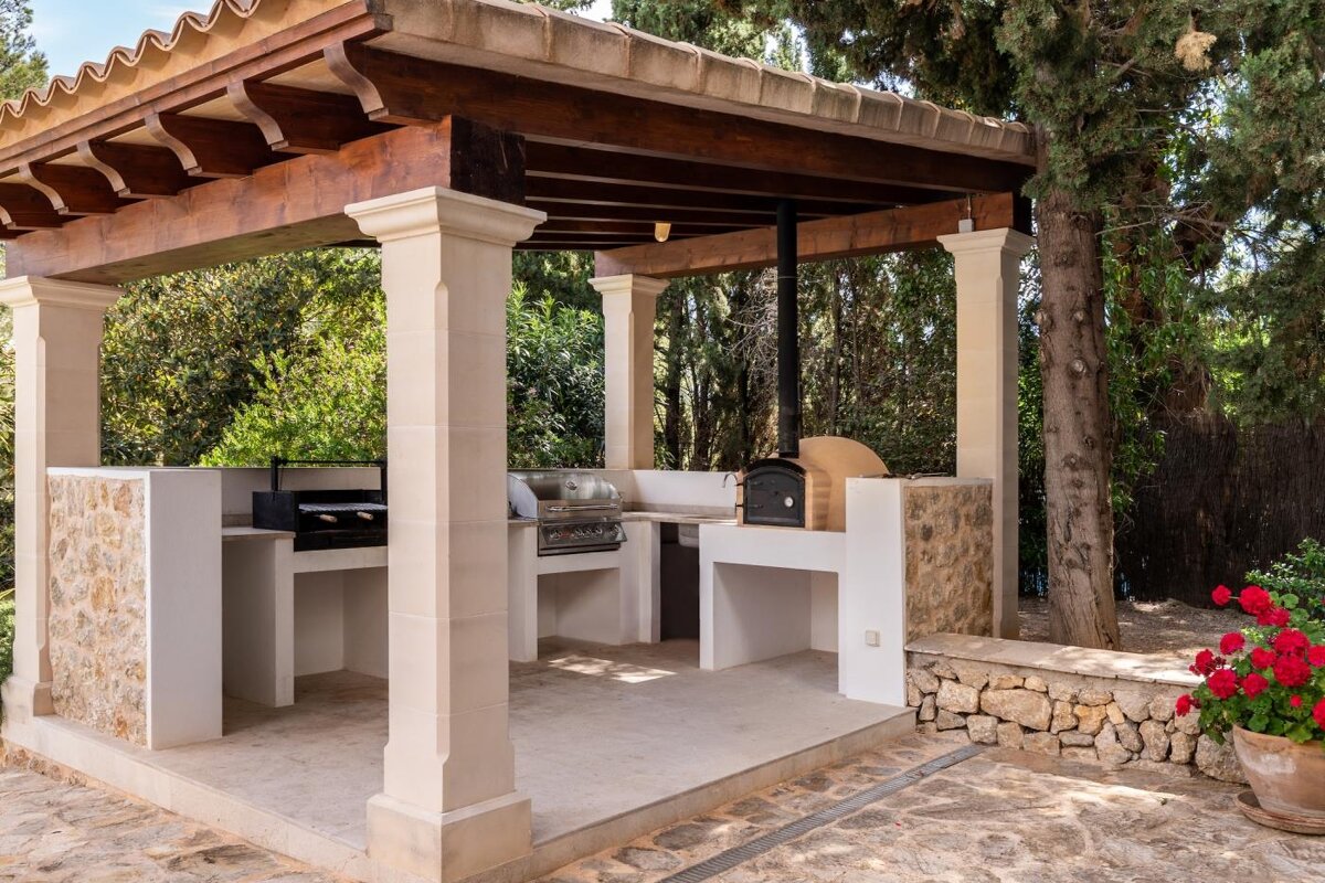 An outdoor kitchen with a grill and oven under a wooden pergola