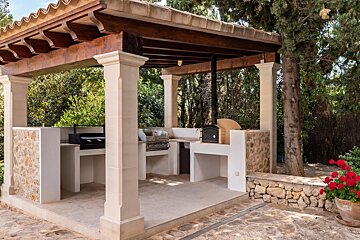 An outdoor kitchen with a grill and oven under a wooden pergola