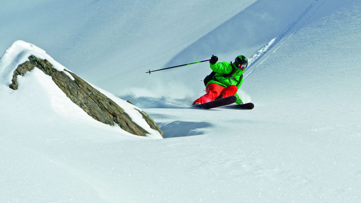 A person in a green jacket and red pants is skiing down a snow covered slope