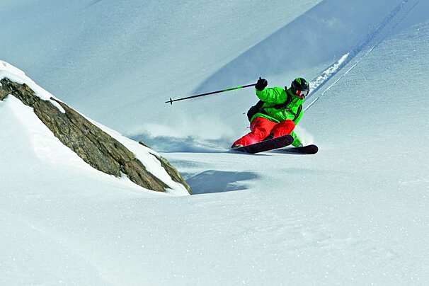 A person in a green jacket and red pants is skiing down a snow covered slope
