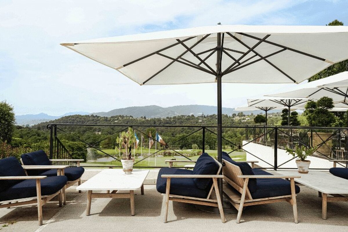 A patio with chairs and tables under umbrellas with mountains in the background