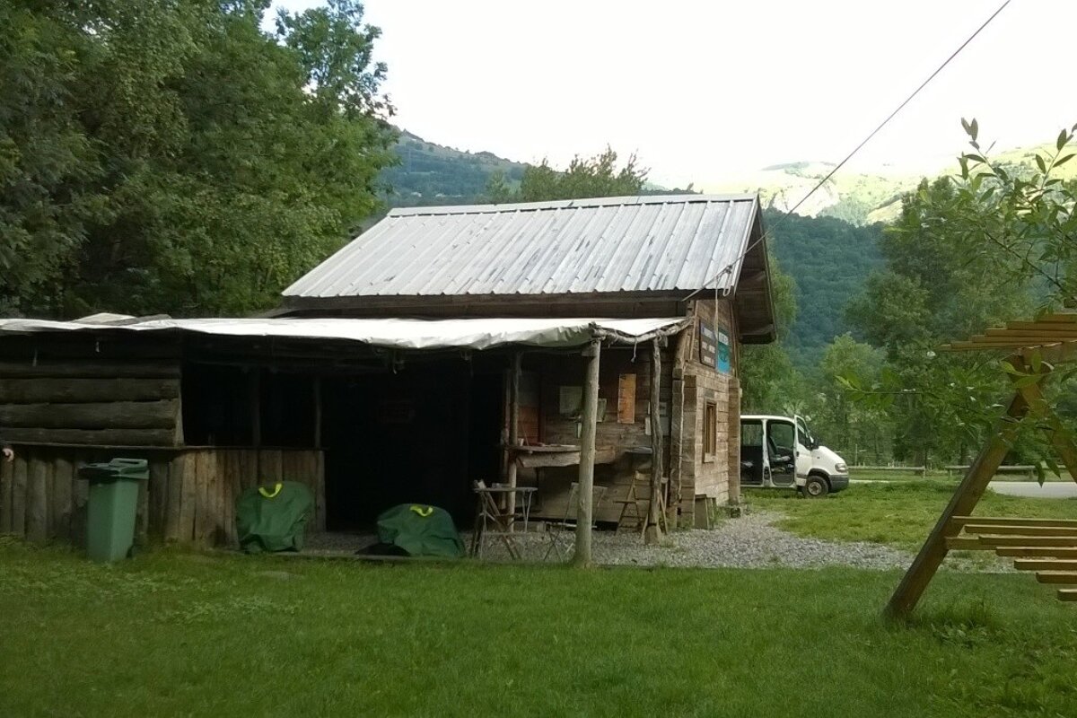 A large wooden hut on some grass with a minibus in the background and some trees