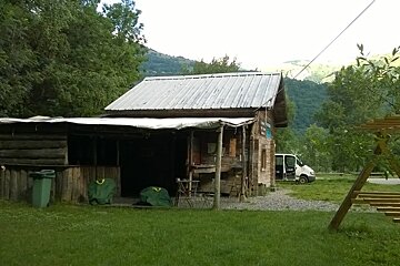 A large wooden hut on some grass with a minibus in the background and some trees