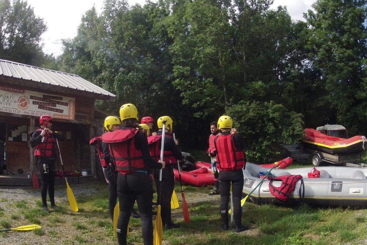 people standing in front of a wooden hut wearing wetsuits and lifejackets with some rafts