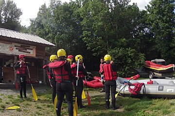 people standing in front of a wooden hut wearing wetsuits and lifejackets with some rafts