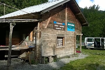 Wooden hut in the sun with a white minibus with its doors open to the right