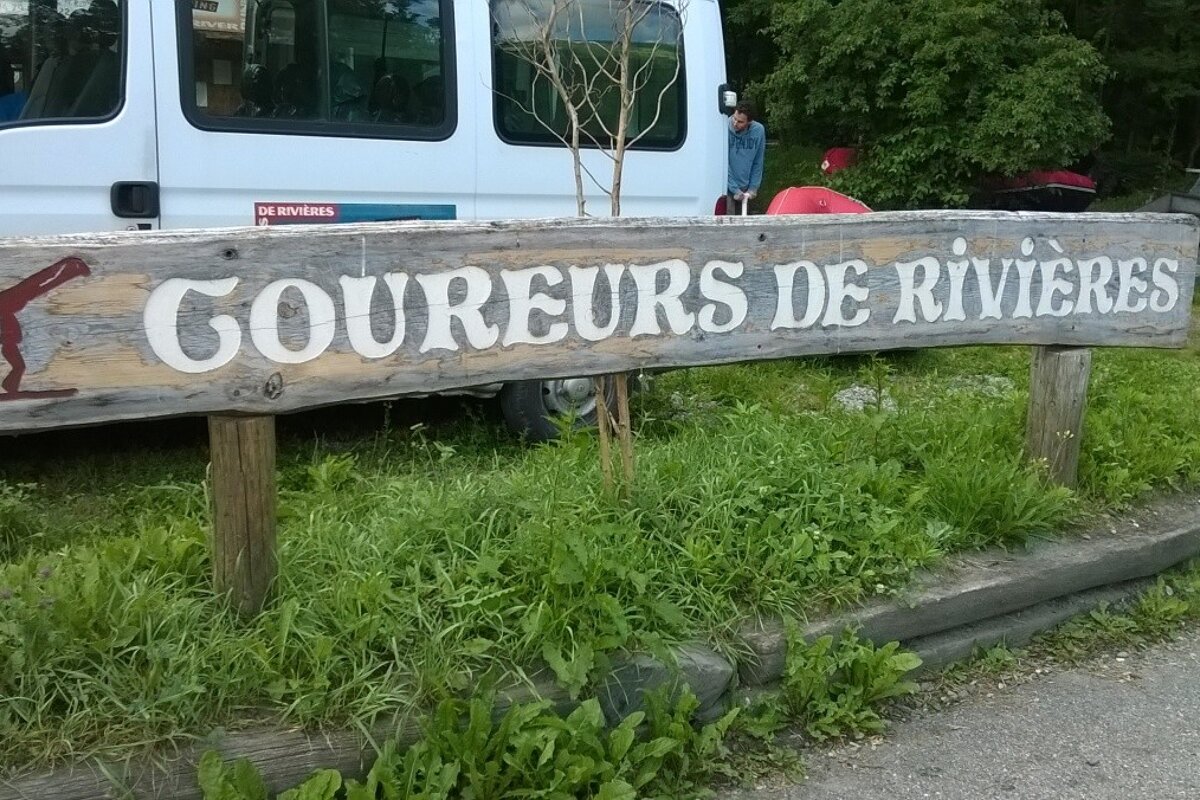 wooden sign saying coureurs de rivières in front of a white minibus
