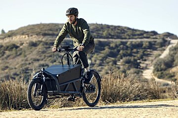A man is riding a cargo bike on a dirt road
