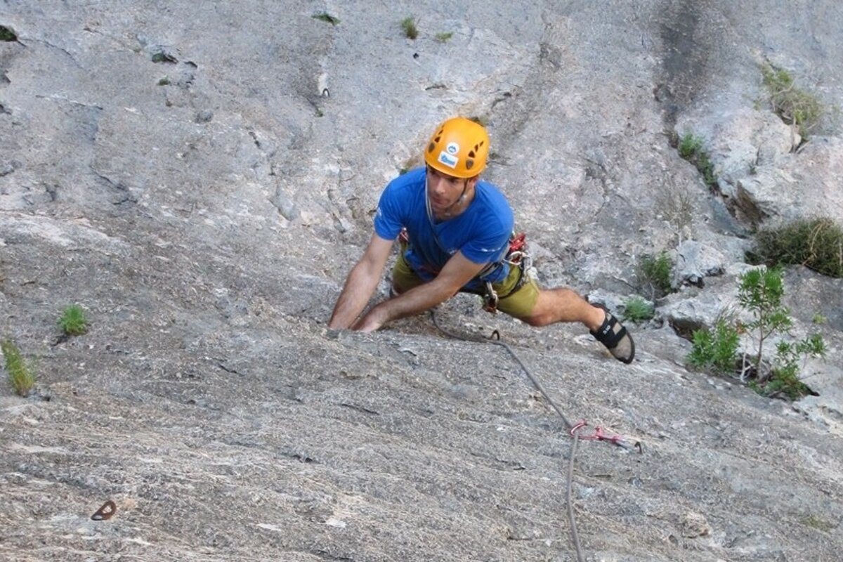 a picture of a man in a yellow helmet climbing a rock face