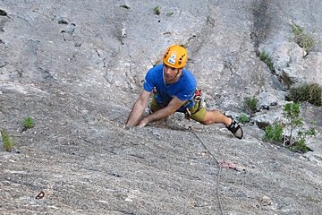 a picture of a man in a yellow helmet climbing a rock face