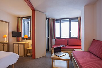 A hotel room with a couch and a laptop on a table