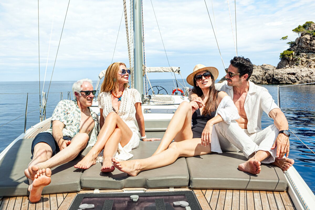 Two couples relax on the deck of a sailboat under a sunny sky, enjoying a scenic ocean cruise.