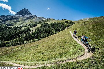 Two people riding bikes on a trail with the words trans savoie on the bottom