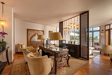 A living room with a desk and chairs and lamps