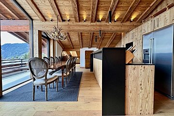 Rustic-modern chalet dining and kitchen area with light wood ceilings, an antler chandelier, a long dining table, and mountain views.