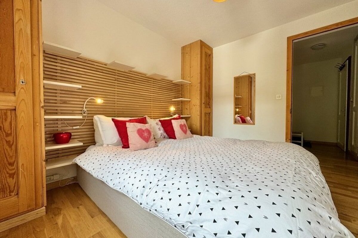 Cozy bedroom with a patterned bedspread, pink heart pillows, and a slatted wooden headboard with integrated shelves.