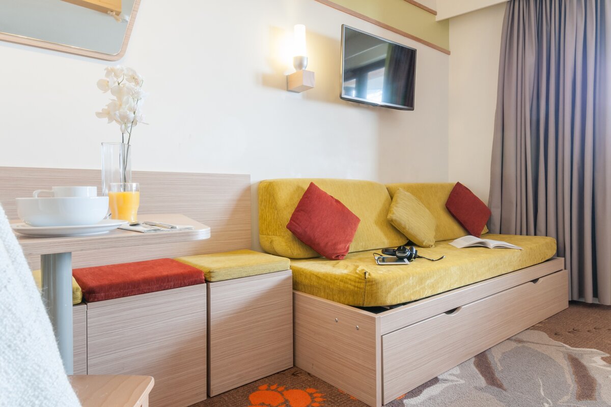A yellow couch with red pillows sits in a hotel room